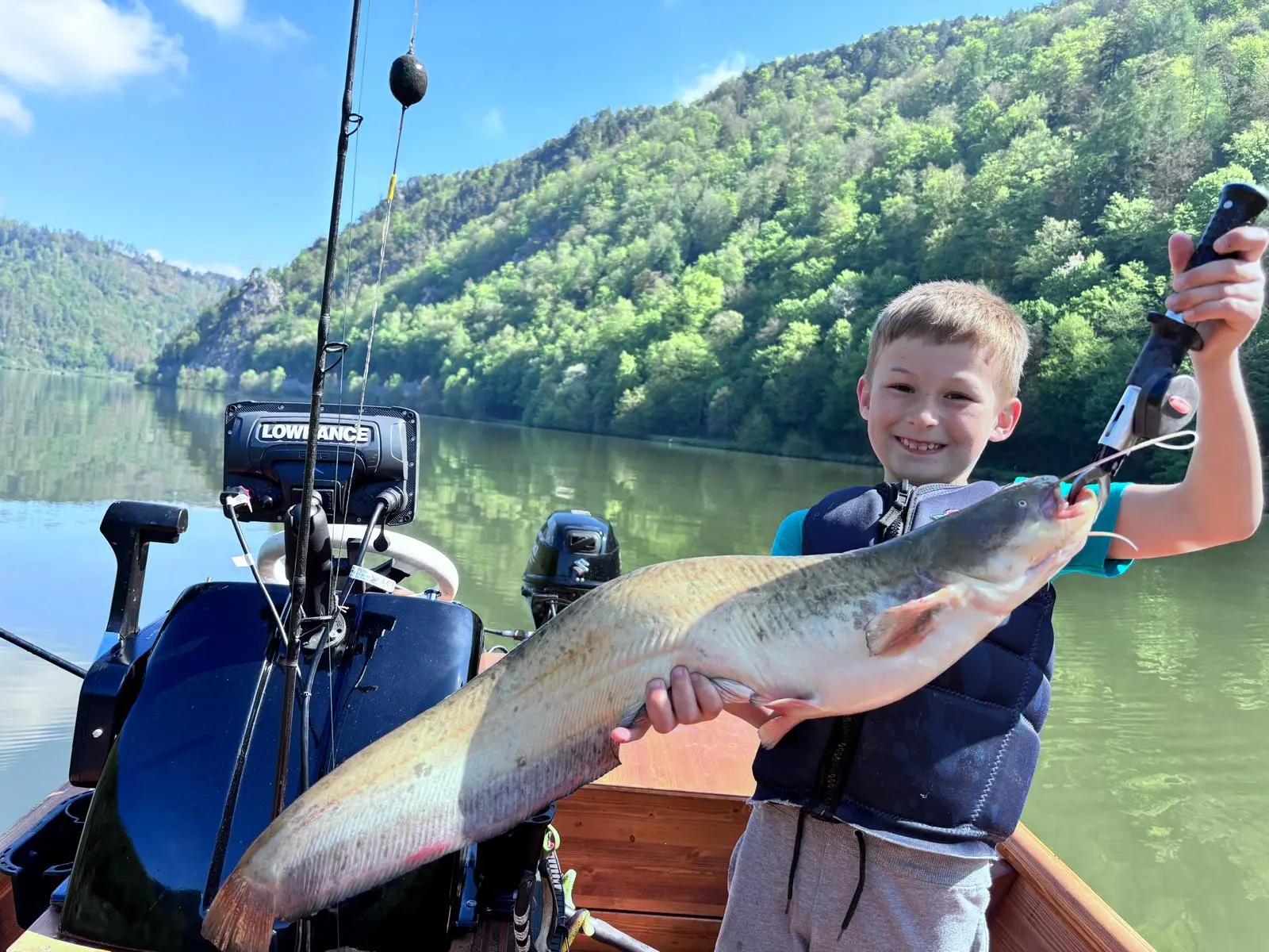 Boy proudly holding his first catfish in the wooden boat on the Danube