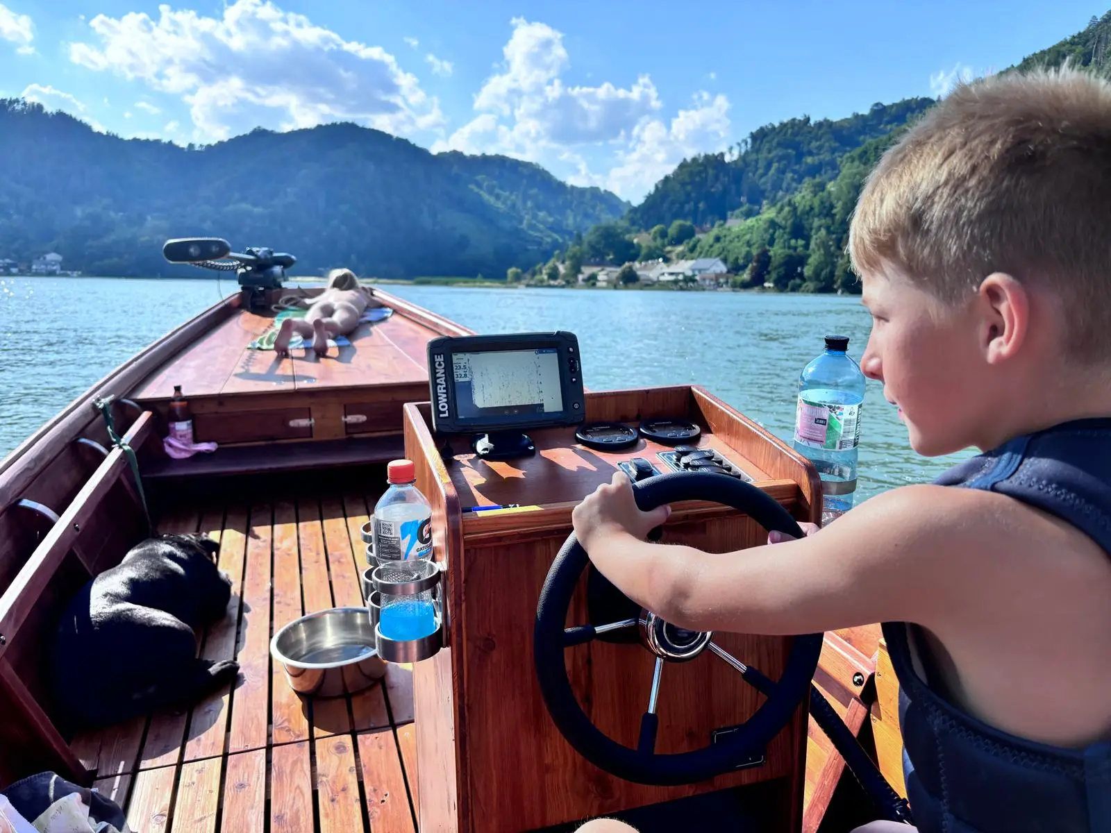 Boy steering the wooden boat and studying the fish finder