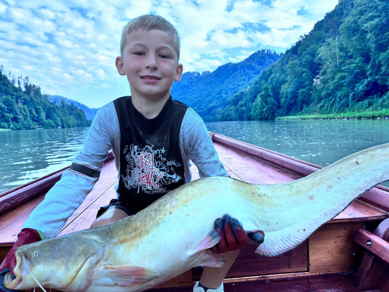 Close-up: proud boy with a big catfish on the wooden boat