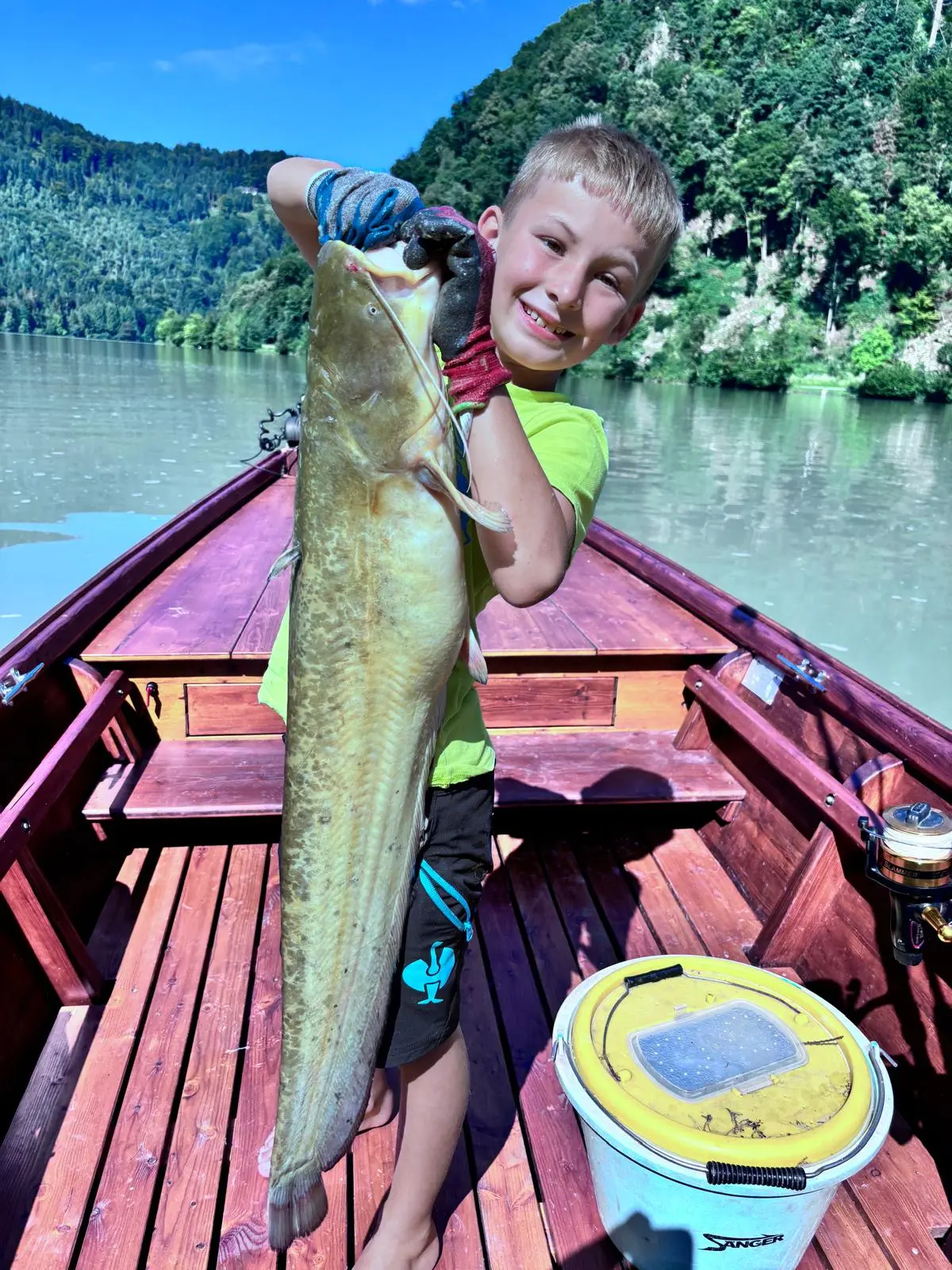 Boy in a neon green shirt presenting his catfish catch