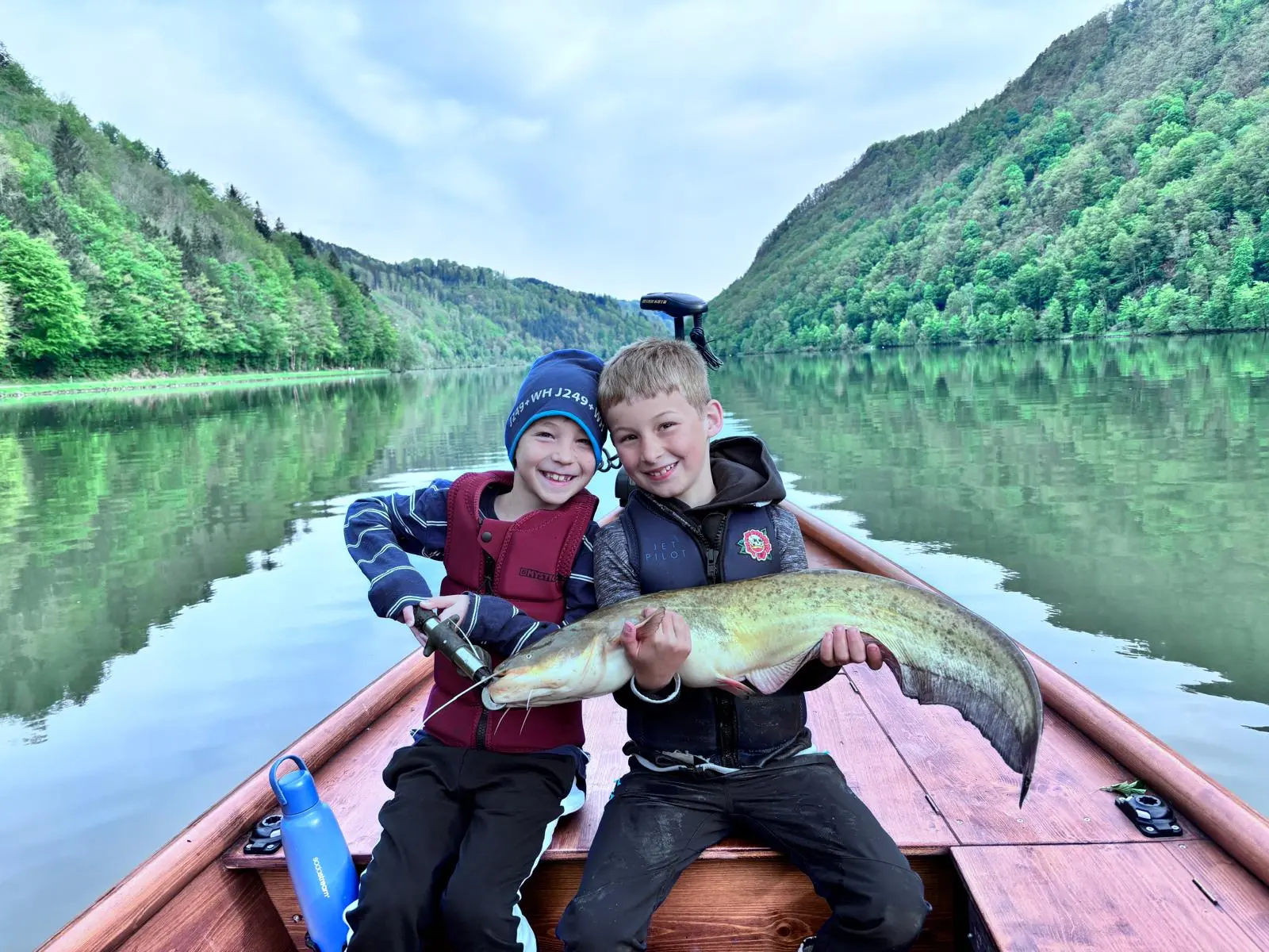 Two boys holding a catfish together, Danube valley panorama in the background