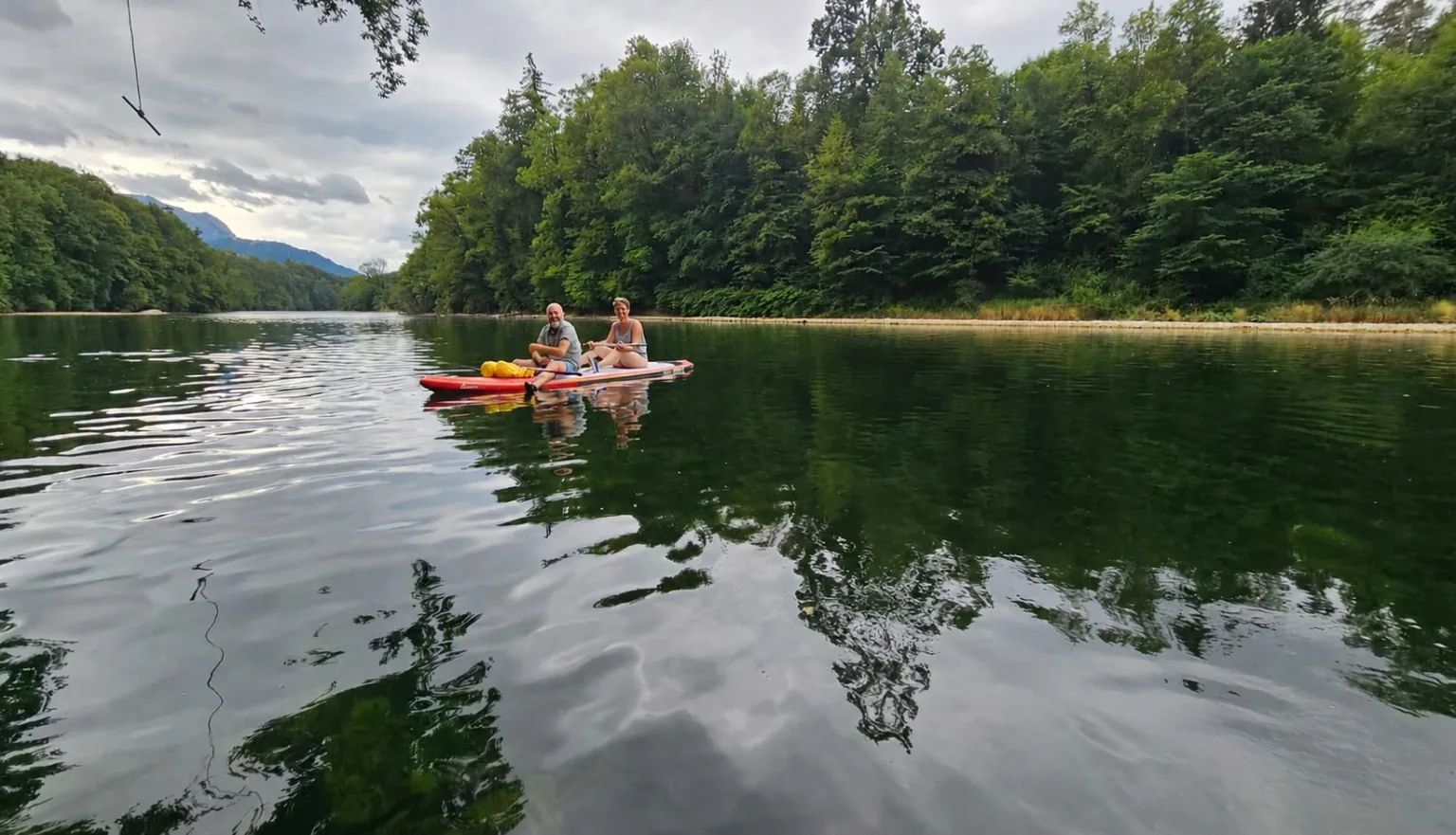 Two people paddling a SUP across a calm green lake